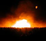 The masses surround the flames and a jellyfish balloon takes flight.