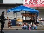 A man with a big gun next to a sausage shack.