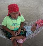 Young girl with her baby sister snuggled into a hammock.