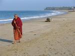 A monk takes a stroll along the beach.