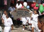 Children march by holding colorful balloons.